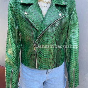 Może przedstawiać: Zielona skórzana kurtka motocyklowa ze skóry węża z zamkiem błyskawicznym. Kurtka ma charakterystyczny wzór i klasyczny styl motocyklowy.