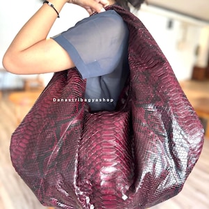 Pode incluir: Uma grande bolsa tote bordô com um padrão de pele de cobra. A bolsa é usada no ombro e parece ser feita de um material texturizado. A bolsa tem um design espaçoso, adequado para transportar vários itens. O texto "Danastribagyashop" é visível.