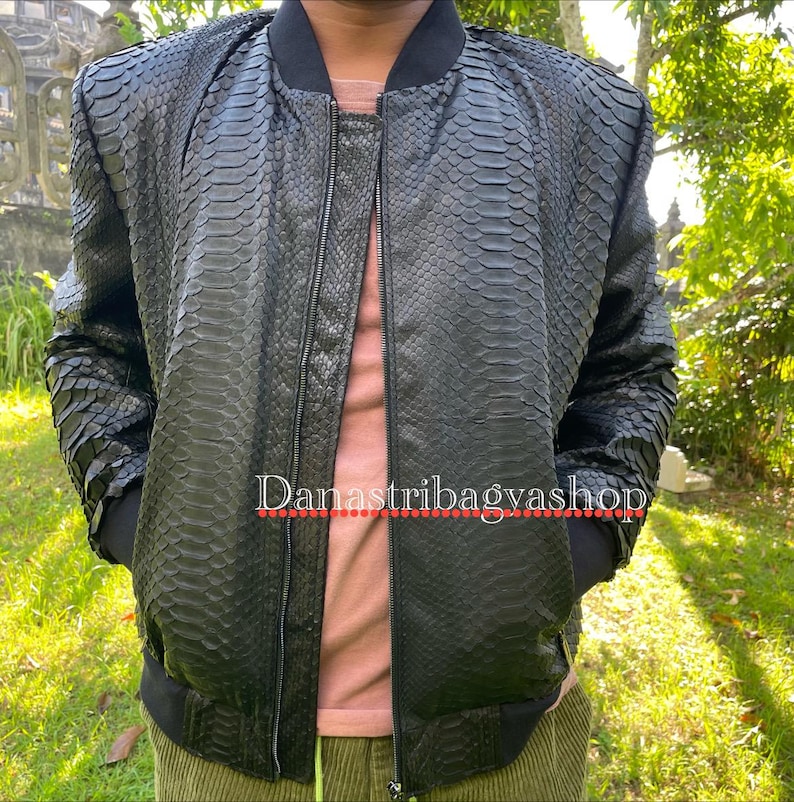 May include: A black bomber jacket made of snakeskin. The jacket has a zip fastening and two pockets. The text "Danastribagyashop" is visible on the jacket.