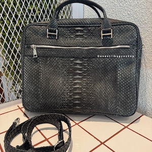 May include: Black briefcase with a snakeskin pattern, featuring a top handle and a detachable shoulder strap. The bag has a silver zipper and hardware. The text "Danastribagyshop" is visible on the bag.