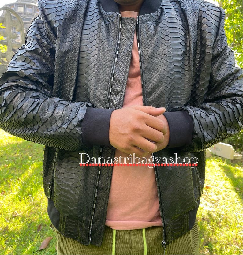 May include: A black bomber jacket made of snakeskin with a zip closure. The jacket has a ribbed collar and cuffs. The text "Danastribavgashop" is visible on the front of the jacket.