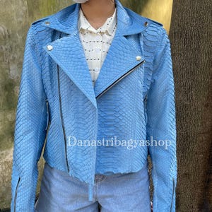 Pode incluir: Uma jaqueta de couro de cobra azul claro com fecho de correr. A jaqueta tem um padrão distinto e um estilo cropped.