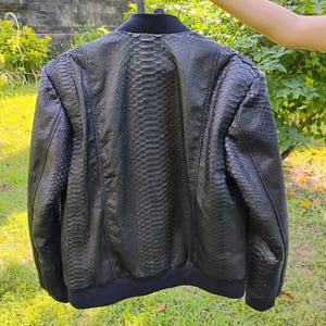 May include: A black leather bomber jacket with a snakeskin pattern. The jacket has a ribbed collar, cuffs, and hem.