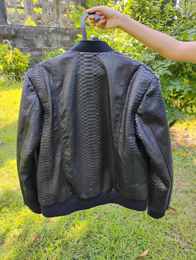 May include: A black leather bomber jacket with a snakeskin pattern. The jacket has a ribbed collar, cuffs, and hem.
