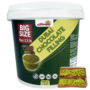 Può includere: Un grande contenitore verde scuro di ripieno al cioccolato di Dubai, con la scritta "BIG SIZE 1kg / 2.2 lb". L'etichetta presenta anche il marchio "güllüoğlu" e le parole "DUBAI CHOCOLATE FILLING". Il contenitore include immagini del ripieno e di una barretta di cioccolato.