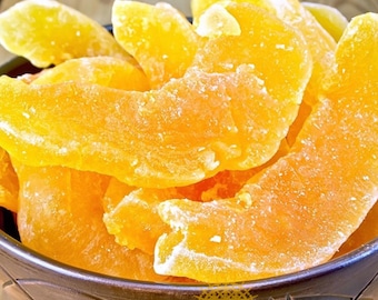 May include: Close-up of dried mango slices in a dark bowl. The mango pieces are a vibrant orange color with a slightly frosted appearance. The bowl has a decorative rim and sits on a wooden surface. The image highlights the texture and color of the dried fruit.
