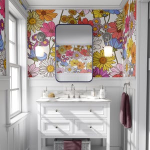 May include: A white bathroom vanity with a marble countertop and a large mirror above it. The walls are covered in a floral wallpaper with a white background and colorful flowers. The vanity has three drawers and a white cabinet below. There is a towel hanging on a rack to the right of the vanity.