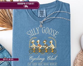 以下が含まれることがあります： 「SILLY GOOSE Cycling Club」の文字と、自転車に乗った4羽のガチョウのイラストが描かれた青いTシャツ。「EAT. SLEEP. RIDE. HONK. REPEAT.」というフレーズも含まれています。