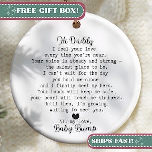 May include: White ceramic ornament with a gold-colored top, featuring the text "Hi Daddy" and a poem about a baby's love. The ornament includes the words "Baby Bump" and a heart symbol.