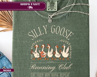 May include: Moss green t-shirt with the words "SILLY GOOSE Running Club" and a graphic of five cartoon geese. The geese are wearing hats and holding drinks. The text "EAT. SLEEP. RUN. HONK. REPEAT." is below the graphic.