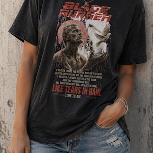 Peut inclure: Un t-shirt noir à manches courtes avec une impression graphique du personnage Roy Batty du film Blade Runner, une colombe en vol et le texte iconique : I've seen things you people wouldn't believe. Like tears in rain. Time to die.