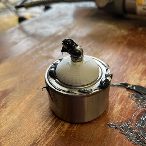 May include: A close-up of a silver bearing with a black rubber seal and a black grease coating. The bearing is sitting on a wooden surface.