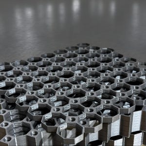 Op de afbeelding: Een stapel grijze, 3D-geprinte zeshoekige vormen, die lijken op een honingraatpatroon.