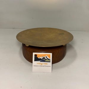 May include: A vintage brass and wood display stand. The stand features a round, brass top and a dark wooden base. A small white label with the text "Vintage Vista Midwest Collected Treasures" is attached to the base.