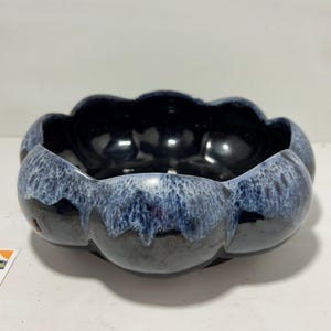 Puede incluir: Un cuenco de cerámica con un diseño de borde festoneado único. El cuenco presenta un interior azul oscuro brillante y un exterior texturizado azul y blanco moteado. La forma del cuenco se asemeja a una flor.