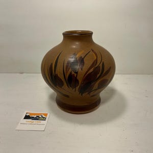 May include: Brown ceramic vase with a rounded body and a flared base. The vase features a hand-painted design of stylized brown and orange leaves. The vase is a decorative item for the home.