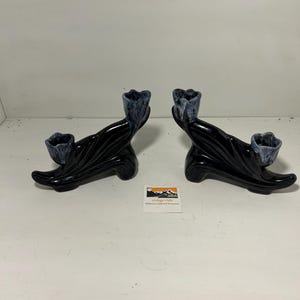 Puede incluir: Un par de candelabros vintage de cerámica negra con acabado brillante. Cada soporte presenta una copa floral azul oscuro estilizada. Los soportes tienen una forma curva y orgánica. Se ve una pequeña etiqueta.