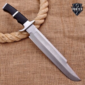 May include: A large, silver-colored knife with a black handle. The knife is lying on a brown burlap surface. The blade is very sharp and has a slight curve to it. The handle is made of a black material and has a silver accent. The knife is about 15 inches long.