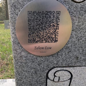 May include: A silver circular plaque with a black and white QR code and the text "Zelon Law -  Our Memories -"