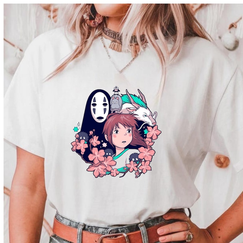 May include: White t-shirt with a vibrant anime-style graphic. The design showcases a girl, a dragon, and other characters amidst pink flowers. The graphic is centrally placed on the front of the tee.