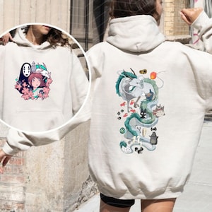 Op de afbeelding: Een beige hoodie met anime-stijl illustraties op de voor- en achterkant. Het ontwerp aan de voorkant toont een meisje, een draak en andere personages. De achterkant toont een draak en andere personages in een verticale opstelling.