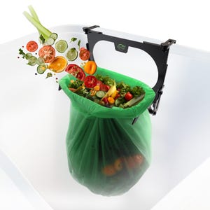 May include: A black metal frame with a green plastic bag hanging from it. The frame is attached to the edge of a white countertop. The bag is filled with various fruits and vegetables, including tomatoes, cucumbers, and lettuce. The fruits and vegetables are flying out of the bag and into the air.