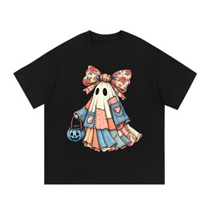May include: A black t-shirt featuring a graphic of a ghost draped in a patchwork quilt of various fabrics, including floral and denim patterns. The ghost wears a large matching floral bow on its head and carries a blue jack-o'-lantern bucket.