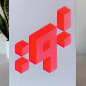 以下が含まれることがあります： 白い背景に、複数の立方体で構成された明るいピンク色の幾何学模様が印刷されています。デザインは、文字の3Dレンダリングを彷彿とさせます。