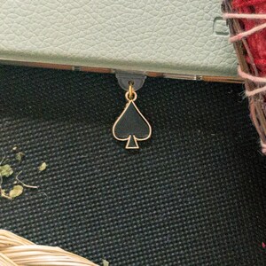 May include: A gold bookmark with a black spade design. The bookmark is hanging from a notebook.