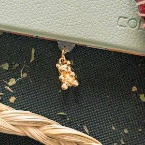 May include: A gold-coloured bear charm with a textured surface hangs from a light green notebook. The charm is made of small, round beads.