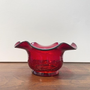 Könnte beinhalten: Eine leuchtend rote Glasschale mit gewelltem Rand und Craquelé-Effekt. Die Schale hat einen dunklen Rand und einen runden Sockel. Die Glasschale ist wahrscheinlich Vintage und für dekorative Zwecke geeignet.