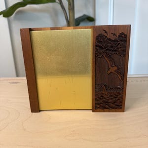 May include: A wooden desk organizer with a brass front panel. The right side features a carved design of an eagle soaring over water and mountains. The organizer is made of dark brown wood.