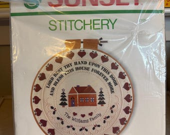 May include: A Sunset Stitchery Christmas Blessing embroidery kit. The kit features a circular design with a house, trees, hearts, and the text "Lord Rest Thy Hand Upon This Door And Bless This House Forever More." The Williams Family is also printed on the design.