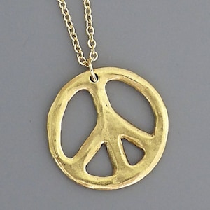 May include: A gold peace sign pendant necklace. The pendant is a simple, open design with a textured surface.