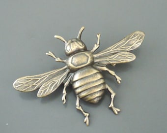 May include: A bronze bee brooch with detailed wings and a textured body.