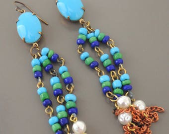 May include: A pair of long, dangling earrings with turquoise blue stones at the top. The earrings feature multiple strands of blue, green, and turquoise beads, with copper chain tassels at the bottom.