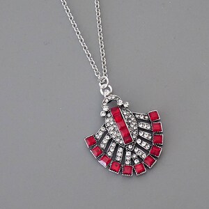 May include: A silver necklace with a red and clear crystal pendant in the shape of a fan.