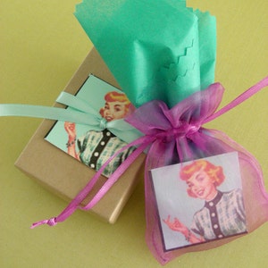 May include: A gift box wrapped in brown paper with a pink ribbon and a vintage illustration of a woman on the front. The box is tied with a pink ribbon and is sitting on a green surface.