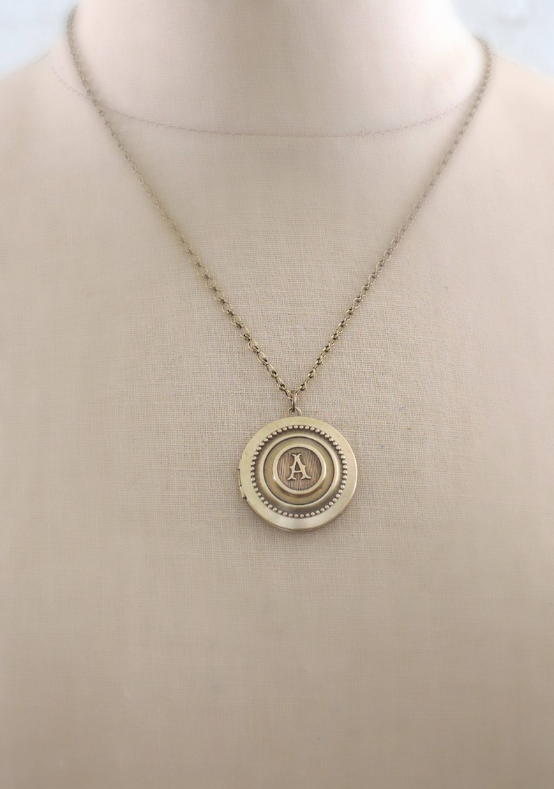 May include: A gold necklace with a round locket pendant featuring the letter "A" in a decorative font.