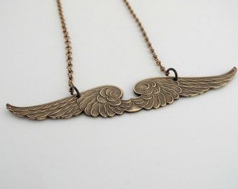 May include: A gold-toned necklace featuring a pendant in the shape of a pair of angel wings. The wings have a textured design.