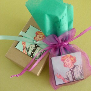 May include: A gift box wrapped in brown paper with a pink ribbon and a vintage illustration of a woman on the front. The box is tied with a pink ribbon and is sitting on a green surface.