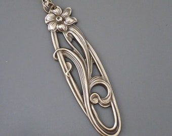 May include: A silver pendant necklace with a floral design. The pendant is shaped like an oval and features a stylized flower with leaves.