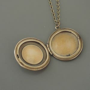 May include: A gold-toned locket necklace with a round, hinged locket. The locket is open, revealing a blank interior.