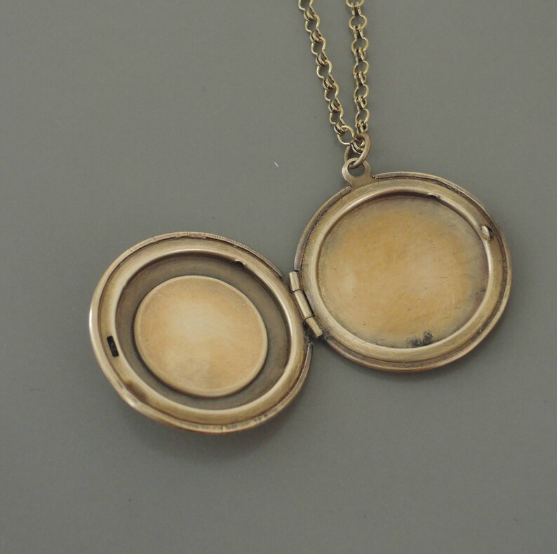 May include: A gold-toned locket necklace with a round, hinged locket. The locket is open, revealing a blank interior.