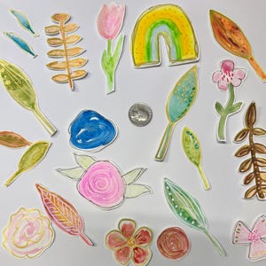 Pode incluir: Ilustrações em aquarela de vários elementos florais e botânicos. A imagem inclui uma tulipa rosa, um arco-íris, folhas e flores em tons de rosa, verde, amarelo e azul. Uma moeda está incluída para escala.