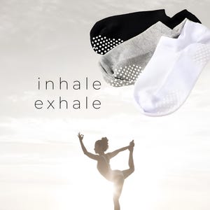 Puede incluir: Tres pares de calcetines invisibles con puntos antideslizantes en la parte inferior. Los calcetines son blancos, grises y negros. El texto "inhale exhale" está escrito en el centro de la imagen.