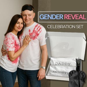 Puede incluir: Un set de celebración de revelación de género. Incluye una caja blanca con una máscara para dormir de satén blanco, dos máscaras para dormir negras y dos bolsas de satén blanco con las etiquetas "Daddy" y "Mommy". El set incluye un tubo con la etiqueta "Boy or Girl". La pareja lleva camisetas blancas con huellas de manos rojas.