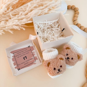 Puede incluir: Un par de patucos para beb&eacute; de peluche en color marr&oacute;n claro con dise&ntilde;o de oso y pu&ntilde;os blancos acanalados, acompa&ntilde;ados de una caja de regalo cuadrada con relleno de papel blanco y una tarjeta con el texto: Grandma and Grandpa, please keep my booties safe. I'll need them back soon.
