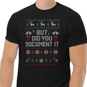 Op de afbeelding: Zwart T-shirt met een feestelijk ontwerp. Het shirt heeft een patroon van rendieren, kerstbomen, sneeuwvlokken en de tekst "BUT DID YOU DOCUMENT IT" in wit en rood. Het shirt is gemaakt van een zacht materiaal.