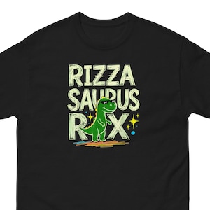 Puede incluir: Camiseta negra con el texto "Rizza Saurus Rex" en una fuente juguetona, con un dinosaurio verde con gafas de sol. El dinosaurio está sobre un diseño colorido de arcoíris.